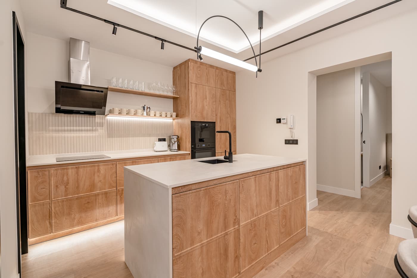 Cocina con isla, frentes en acabado madera y lámpara lineal curva. Atocha 111, Madrid.