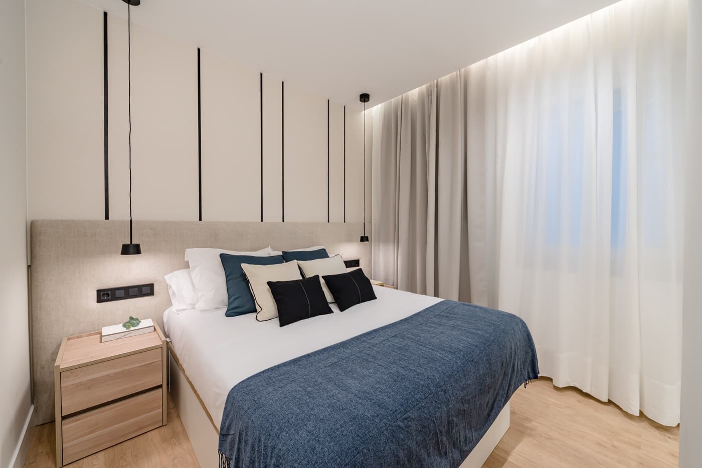 Dormitorio con cabecero tapizado, listones negros en la pared y cortinas de suelo a techo. Atocha 111, Madrid.