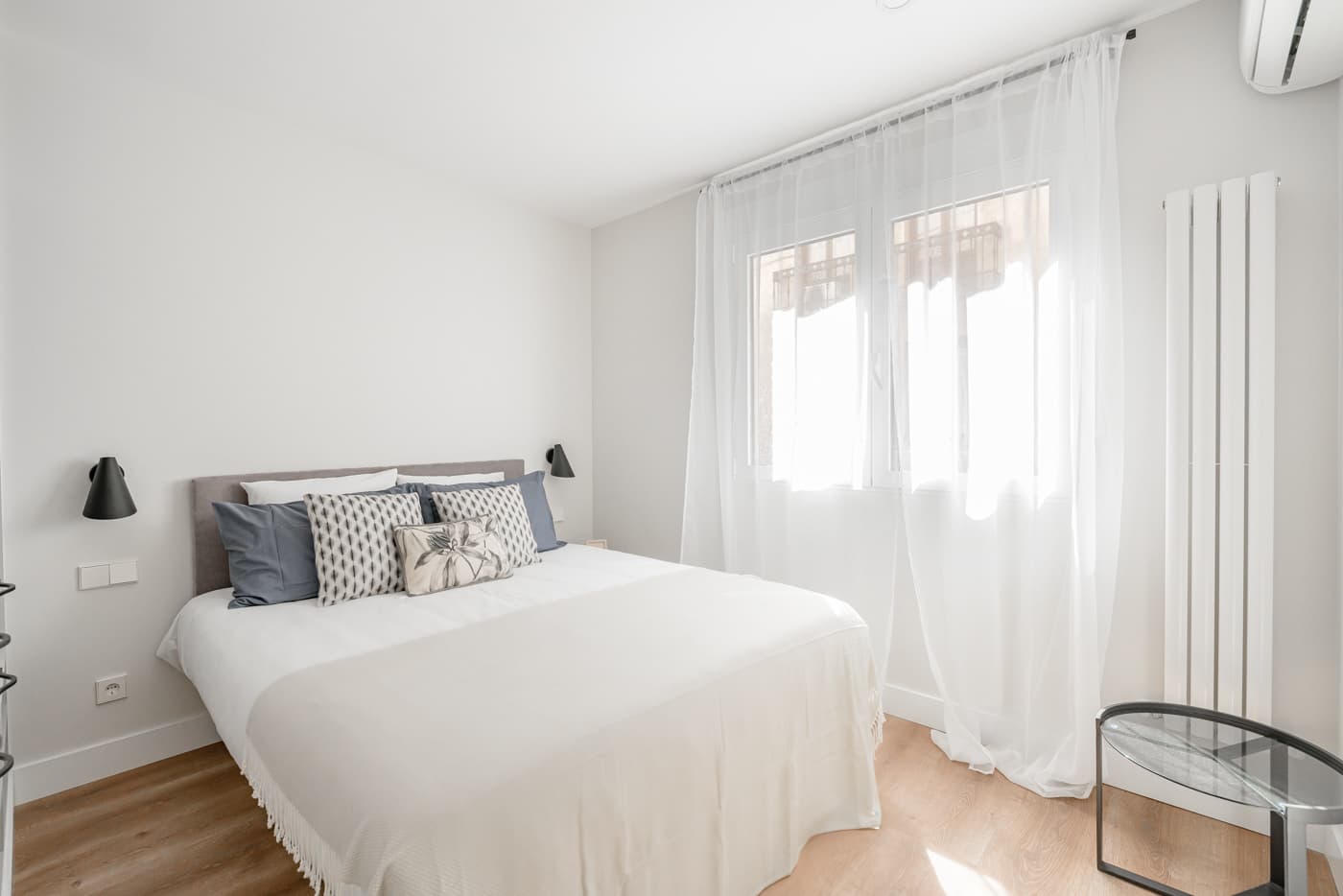 Dormitorio con ventana, visillos y radiador vertical blanco. Atocha 94, Madrid.