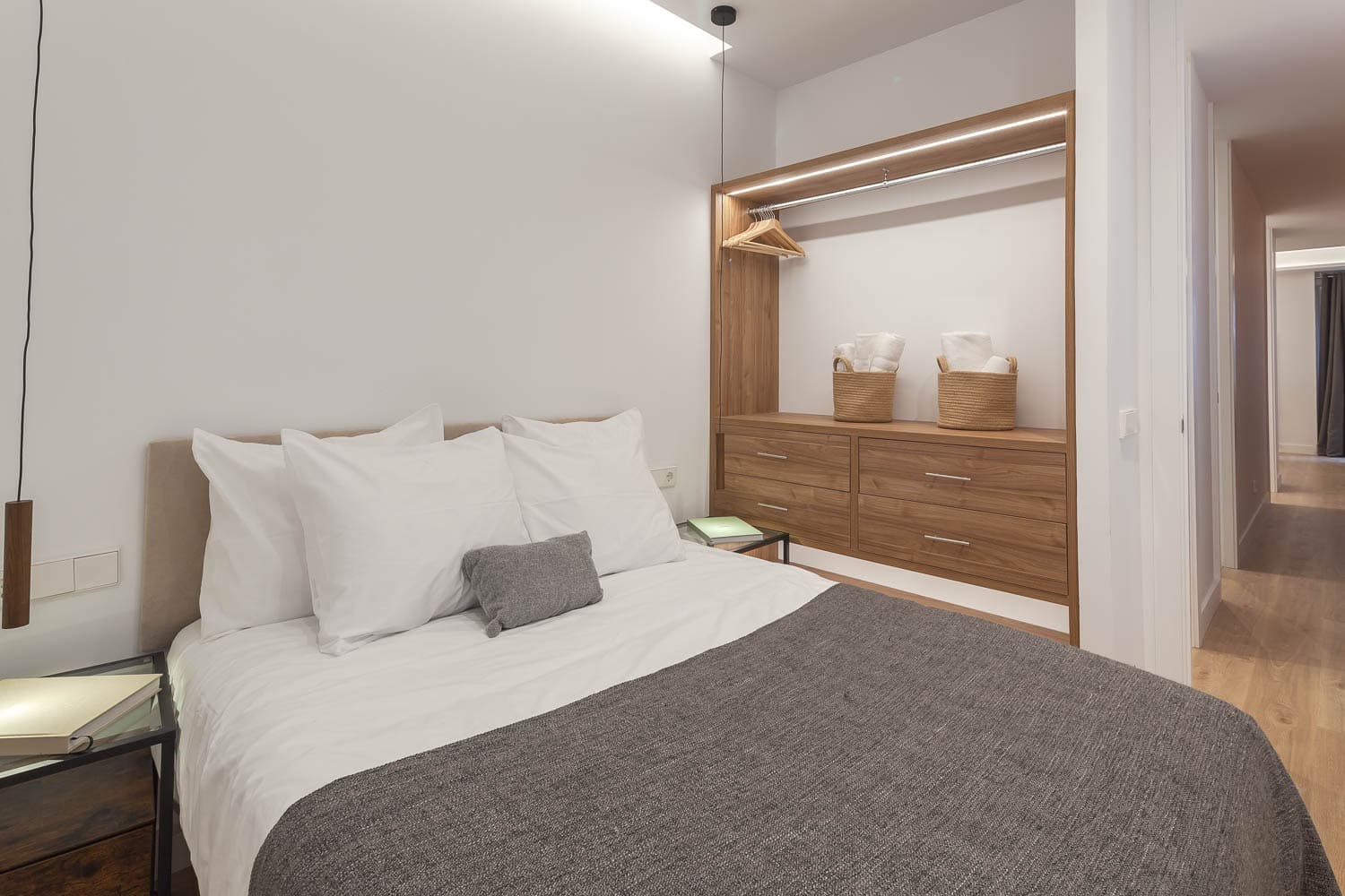 Dormitorio con armario abierto en acabado madera y luz integrada. Cisneros, Madrid.