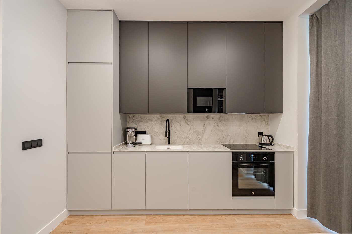 Cocina lineal con muebles altos oscuros, columnas claras y frente veteado. Divino Pastor 14, Madrid.
