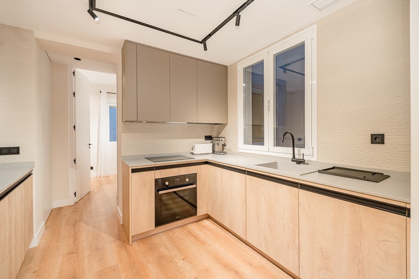 Cocina en L con frentes en acabado madera clara, encimera gris y carril de focos en el techo. Hermosilla 133, Madrid.