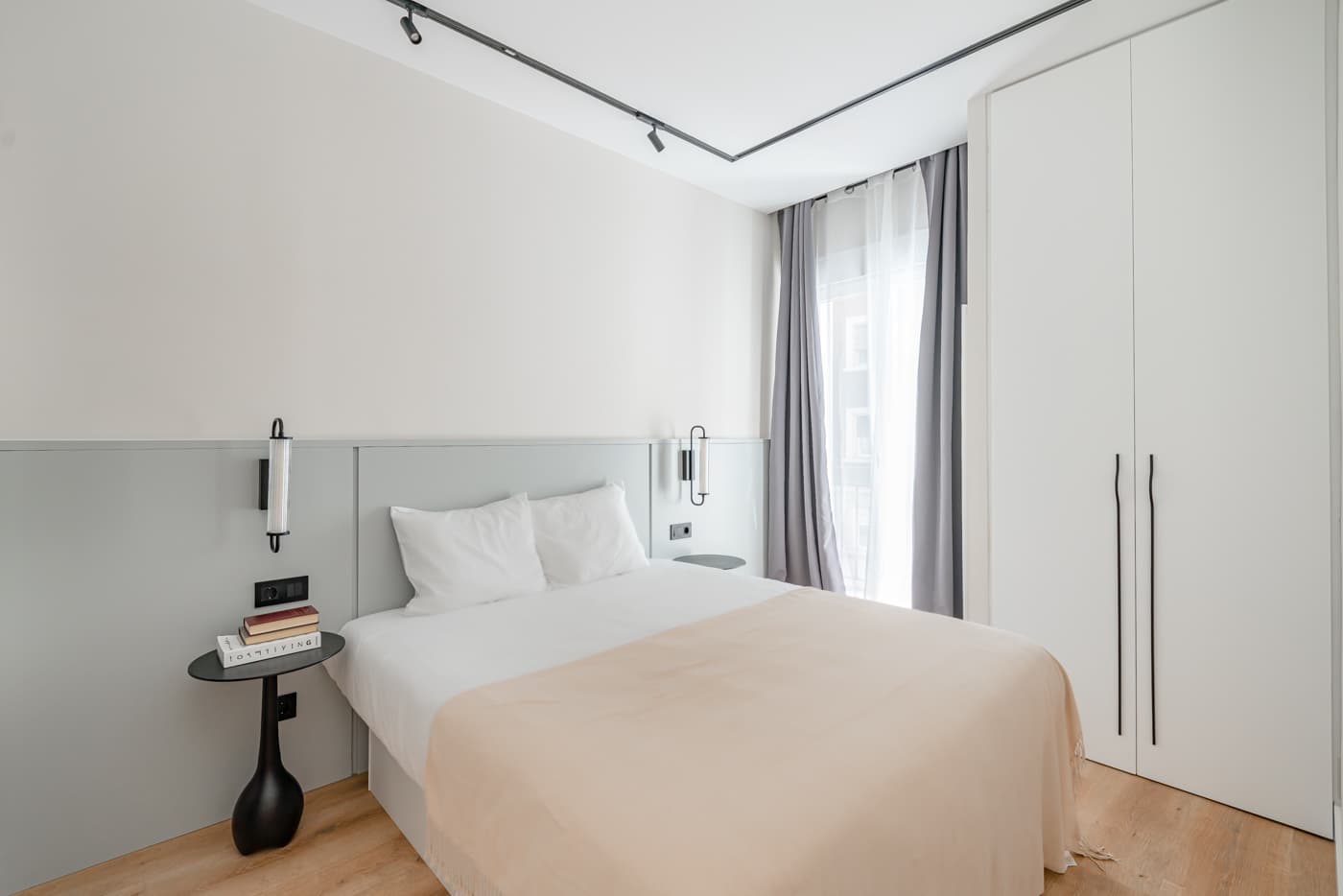 Dormitorio con armario blanco de suelo a techo, zócalo gris tras la cama y carril de focos. Hermosilla 133, Madrid.