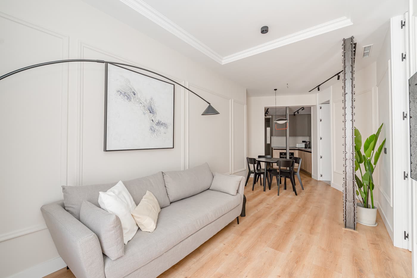 Salón con sofá gris y lámpara de arco; al fondo, el comedor y la columna de acero vista. Hermosilla 133, Madrid.