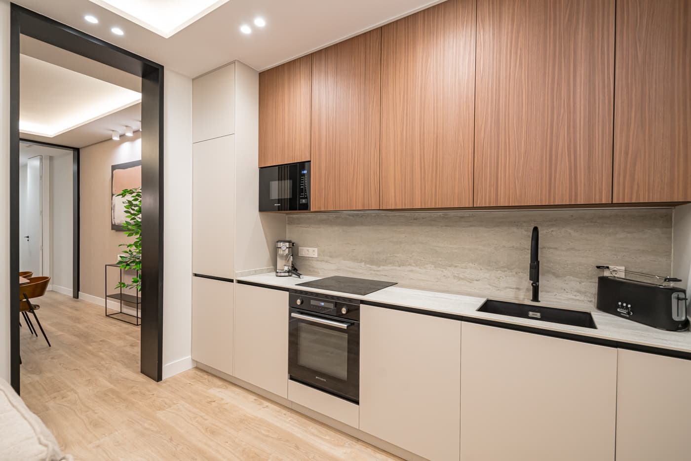 Cocina lineal con muebles altos en acabado madera, frente veteado y paso con marco negro al comedor. Jesús del Valle 25, Madrid.