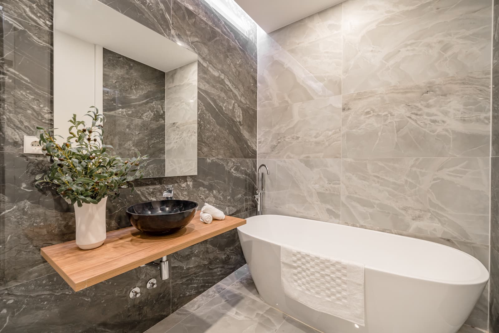 Baño con bañera exenta, revestimiento gris veteado y lavabo negro sobre encimera de madera. Lagasca 136, Madrid.