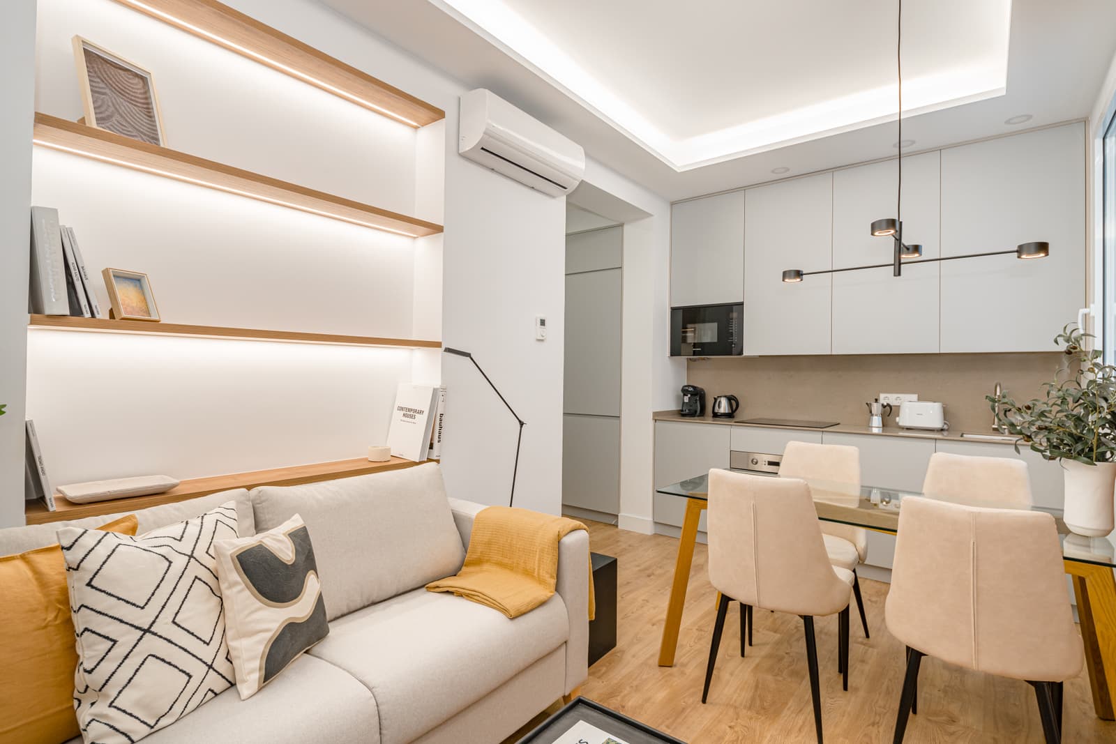 Salón con sofá y estantes con luz integrada; al fondo, la mesa y la cocina. Lagasca 136, Madrid.