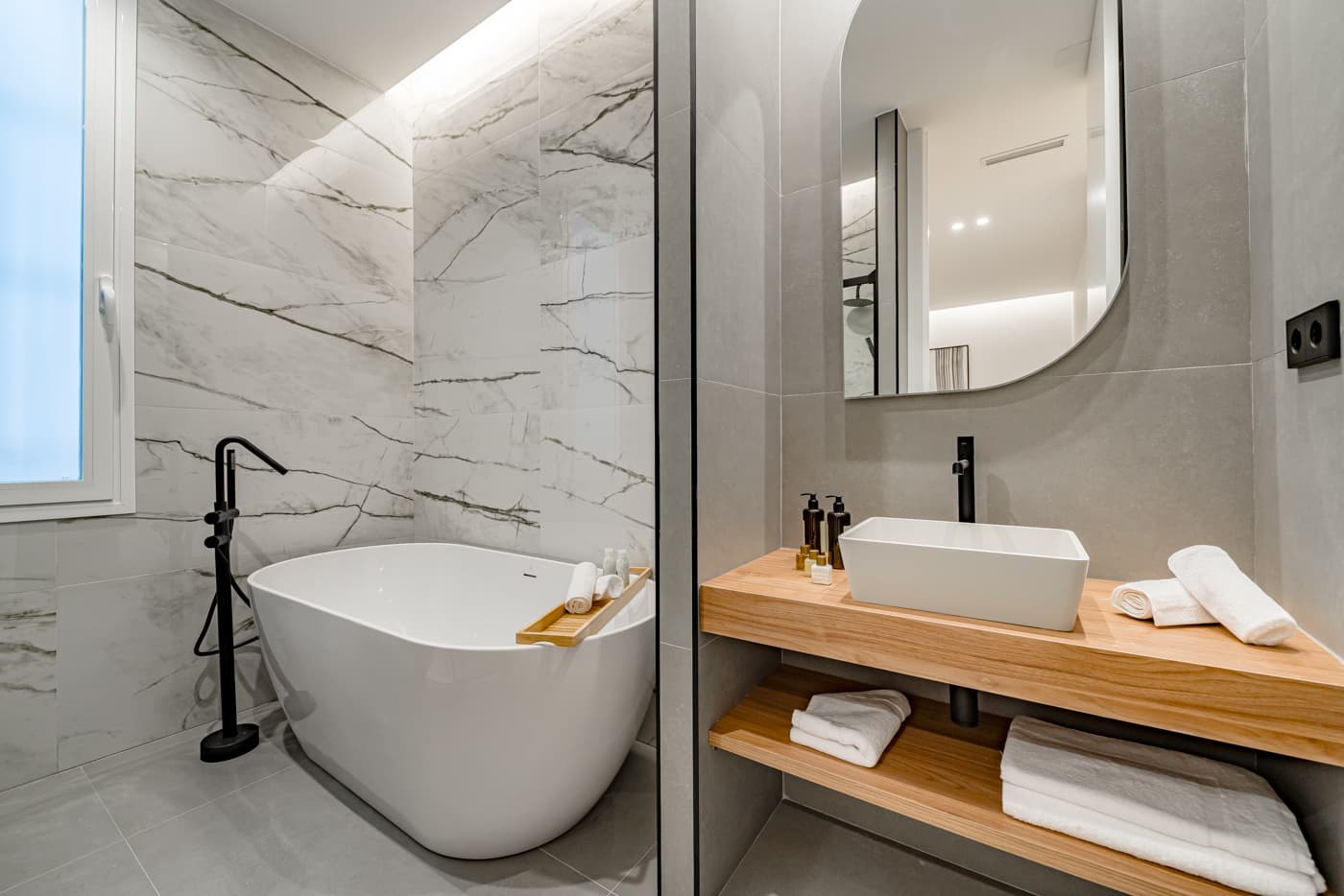 Baño con bañera exenta, grifería negra de pie y lavabo sobre encimera de madera. Plaza de Santa Bárbara 6, Madrid.
