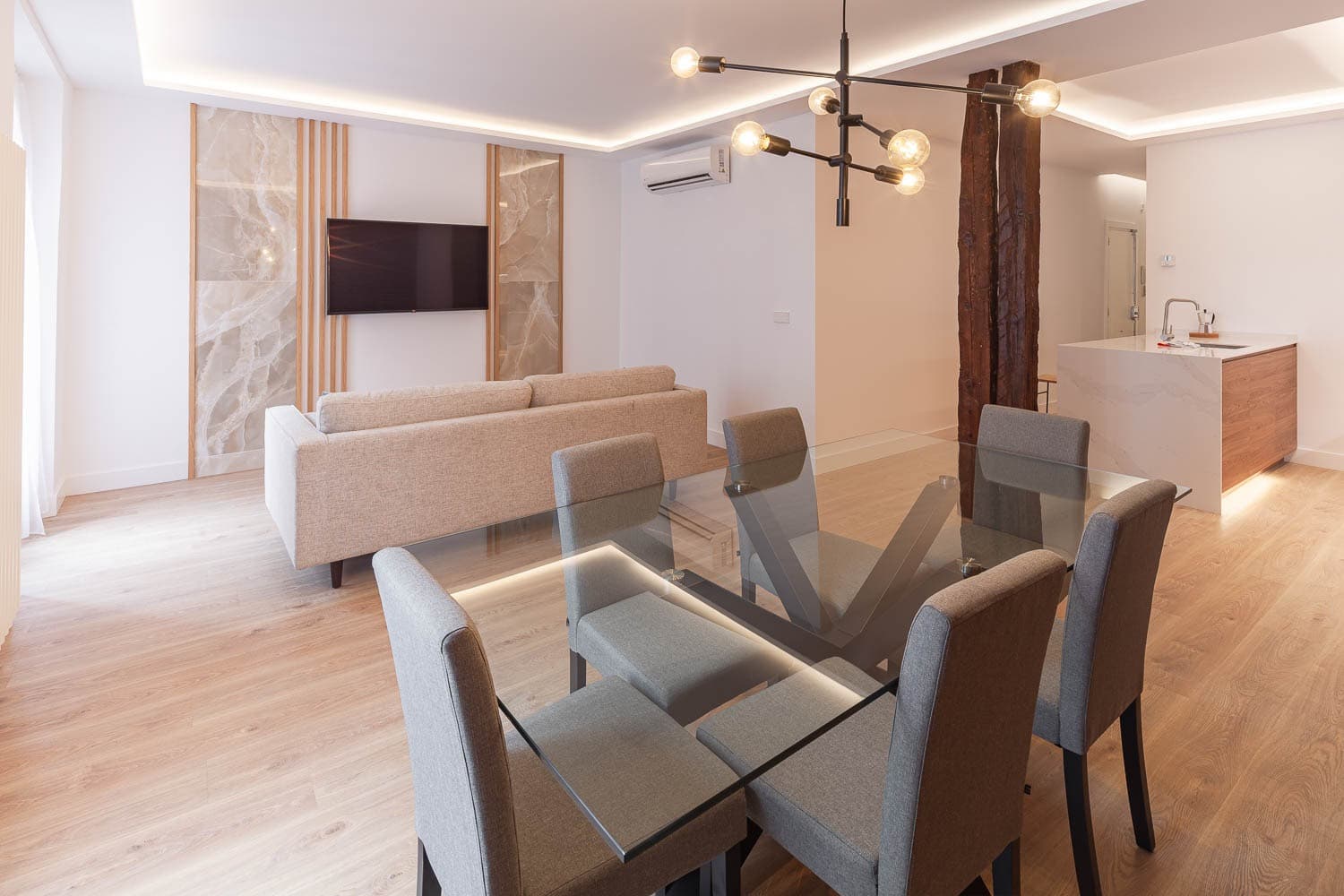 Mesa de cristal en primer plano; al fondo, el salón, un pie derecho de madera y la cocina. Calle Ruiz, Madrid.