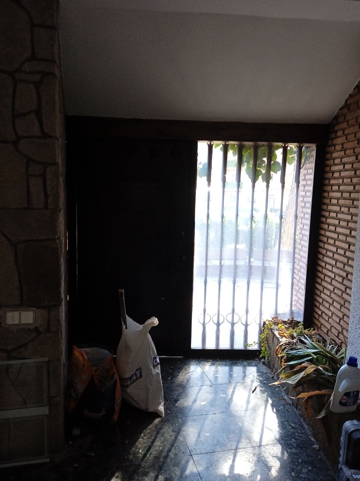 La entrada antes de la obra, en penumbra, con el muro de piedra y la puerta de reja.