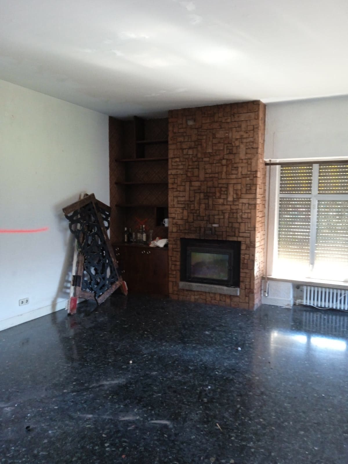 El salón antes de la obra: suelo oscuro y la chimenea de ladrillo original, sin revestir.