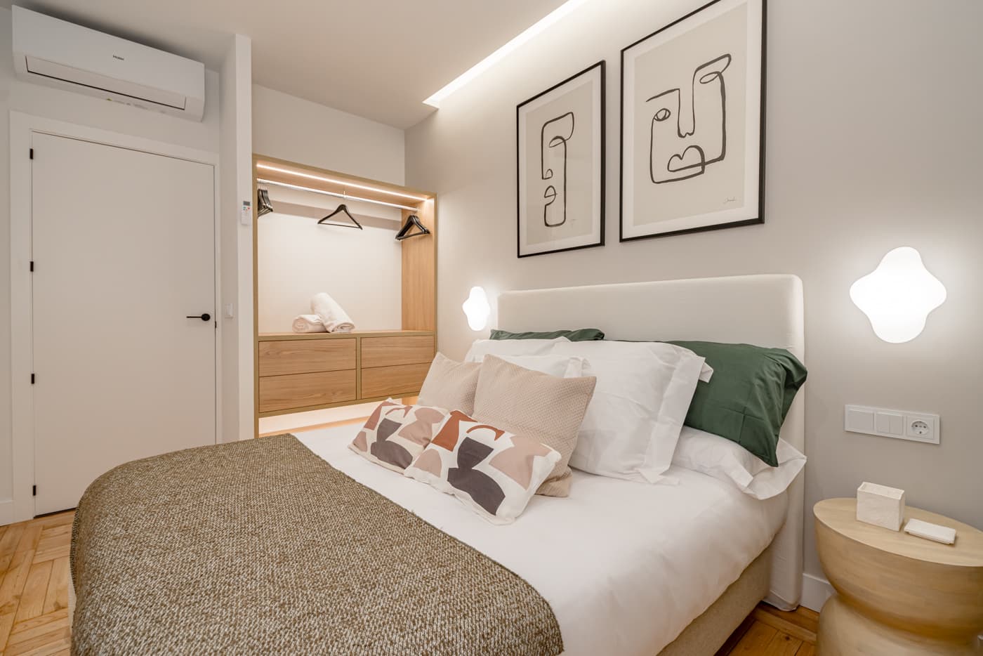 Dormitorio con armario abierto en acabado madera y luz indirecta en el techo. Vía Complutense, Alcalá de Henares.