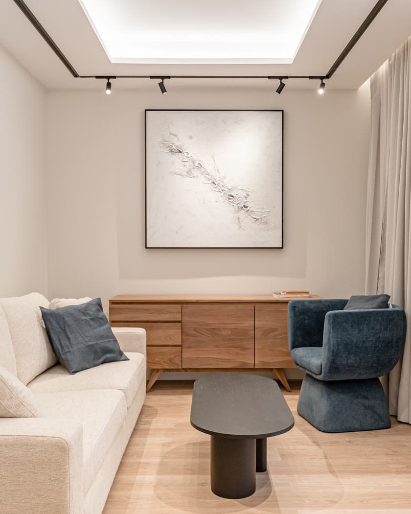 Salón con sofá claro, butaca azul y aparador de madera
