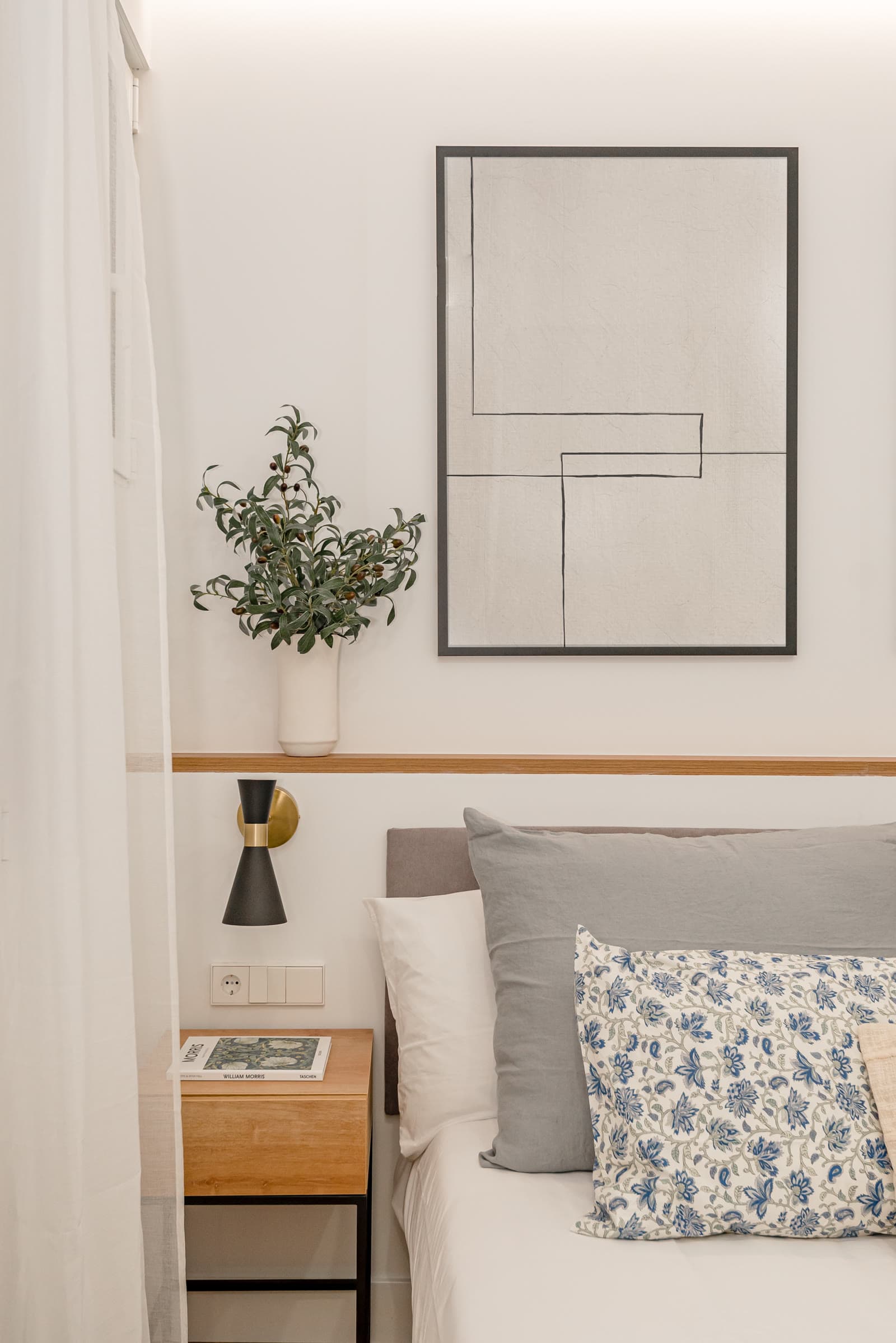 Dormitorio con cuadro de líneas, cojín estampado y aplique de pared