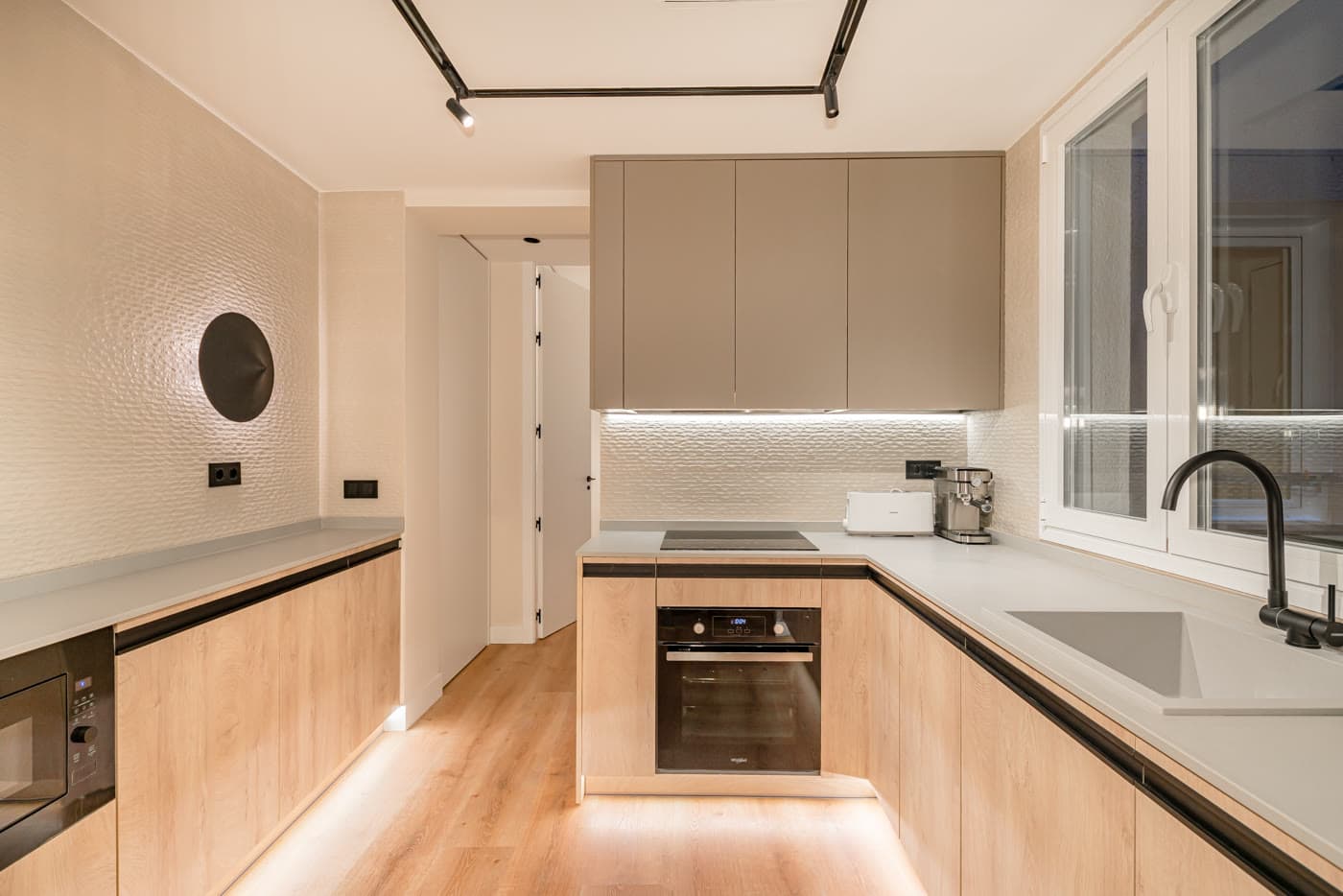 Cocina con frentes de madera, encimera clara y espejo redondo iluminado