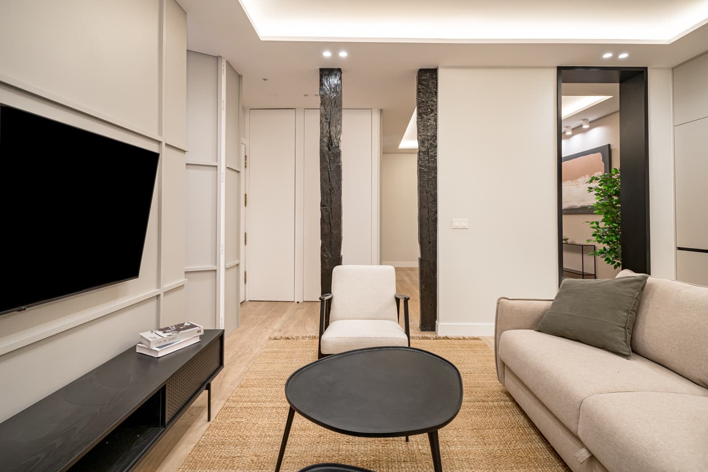 Salón con dos pies derechos de madera antigua a la vista entre el sofá y la entrada. Jesús del Valle 25, Madrid.
