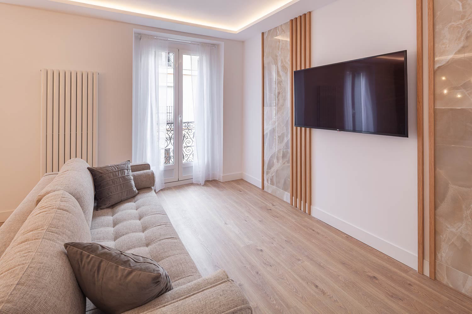 Salón reformado con sofá, radiador vertical, balcón y paneles de madera